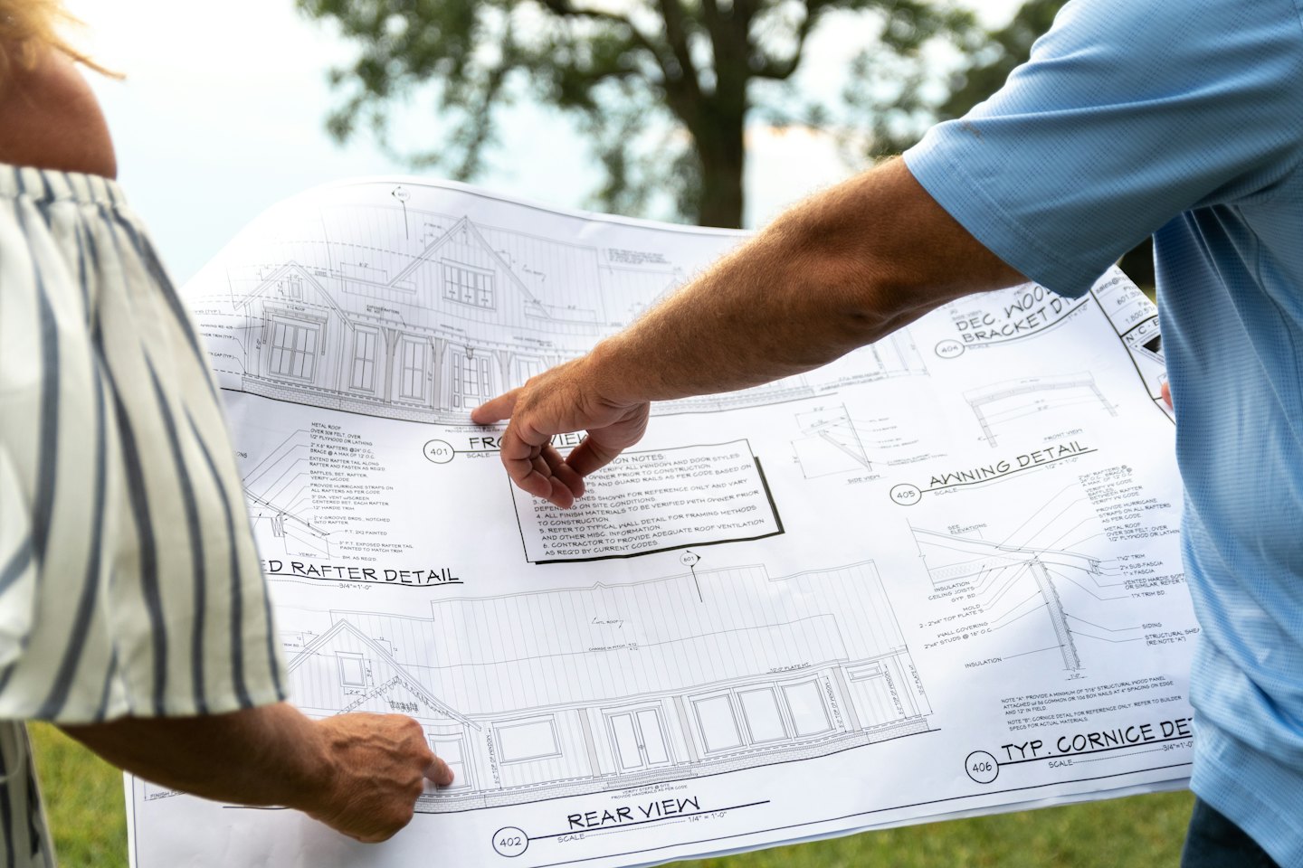 Dwie osoby omawiają plany architektoniczne domu, stojąc na zewnątrz.